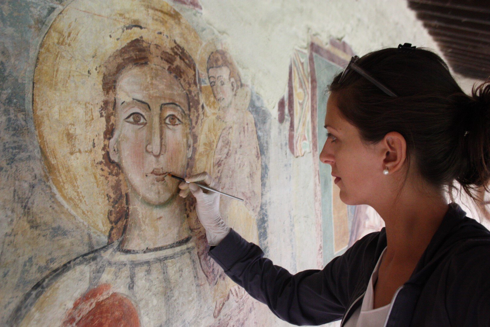 Eleonora Cigognetti al lavoro sul restauro di un dipinto murale raffigurante un volto sacro